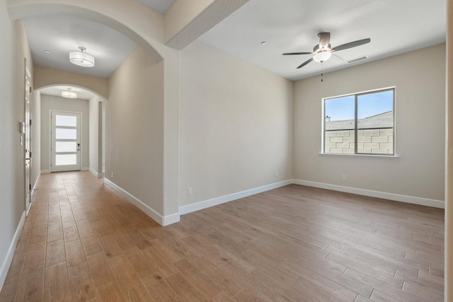 empty room with arched walkways, light wood-style flooring, a ceiling fan, and baseboards