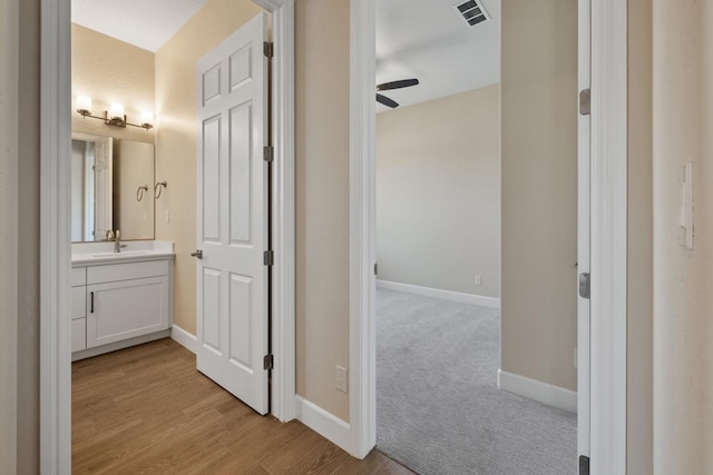 hall featuring a sink, baseboards, and light wood finished floors