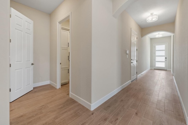 hall with arched walkways, light wood finished floors, and baseboards