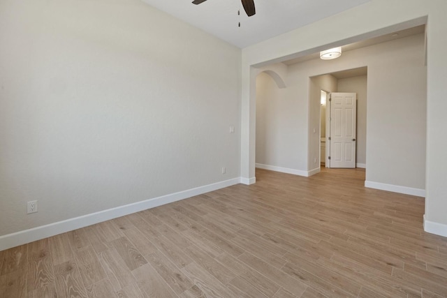 spare room featuring a ceiling fan, arched walkways, light wood-type flooring, and baseboards