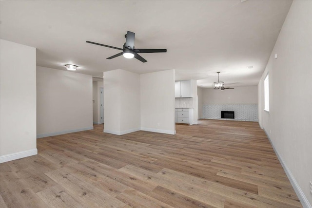 5706 N Tamera Ave, Fresno, CA 93711 - unfurnished living room featuring a ceiling fan, light wood-style floors, a tiled fireplace, baseboards, and a chandelier