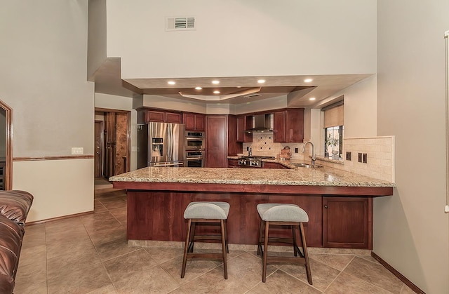 1025 E Cambridge Ave, Visalia, CA 93292 - kitchen with appliances with stainless steel finishes, wall chimney range hood, a peninsula, light stone counters, and a towering ceiling