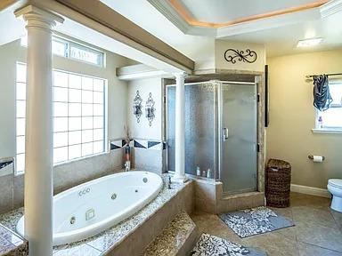 full bath featuring decorative columns, a stall shower, a tub with jets, and toilet