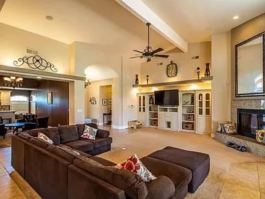 tiled living room with a glass covered fireplace, ceiling fan, high vaulted ceiling, and beamed ceiling