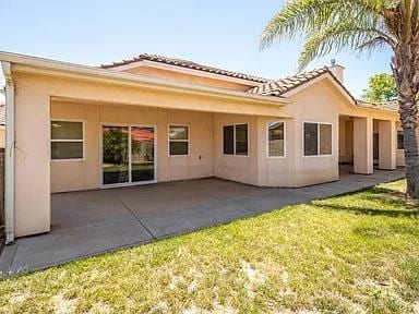 rear view of house with stucco siding, a tiled roof, a yard, and a patio area