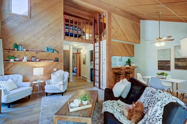 living area with a high ceiling, wooden walls, wood finished floors, and a ceiling fan