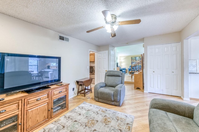 living room featuring ceiling fan, a textured ceiling, light wood finished floors, washer / dryer, and baseboards