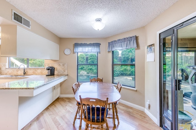 dining room with light wood-style flooring, healthy amount of natural light, a textured ceiling, and baseboards