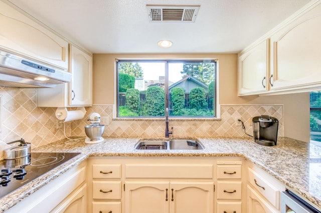 kitchen featuring black electric cooktop, under cabinet range hood, a sink, beverage cooler, and decorative backsplash