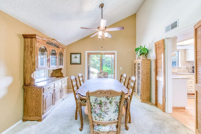 dining space with vaulted ceiling, ceiling fan, light carpet, a textured ceiling, and baseboards