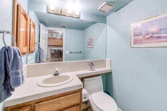bathroom featuring independent washer and dryer, toilet, vanity, and a textured wall