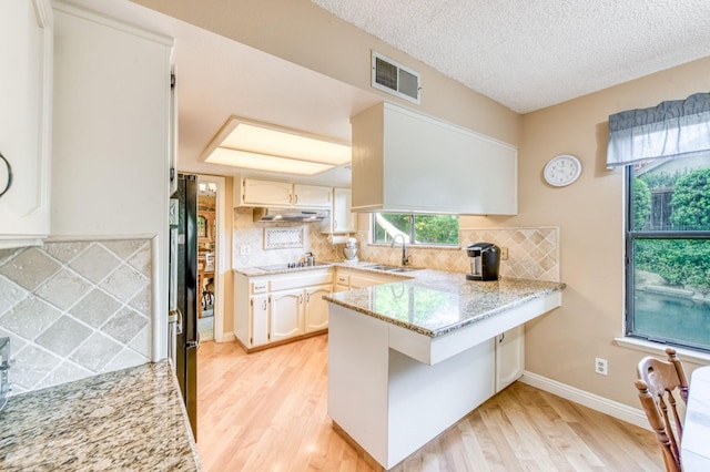 kitchen with a peninsula, light wood-type flooring, under cabinet range hood, backsplash, and a textured ceiling