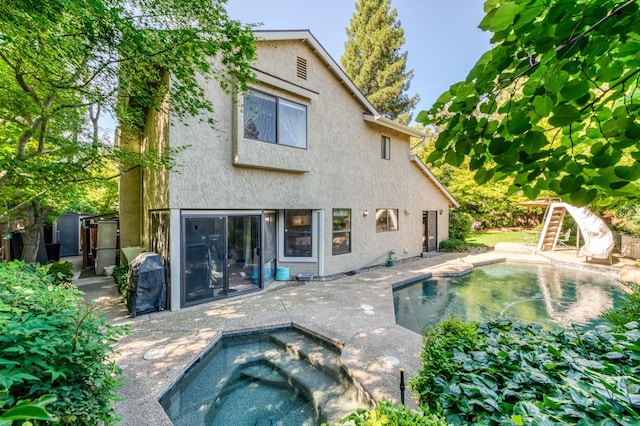 rear view of house featuring stucco siding, an in-ground hot tub, an outdoor pool, and a patio area