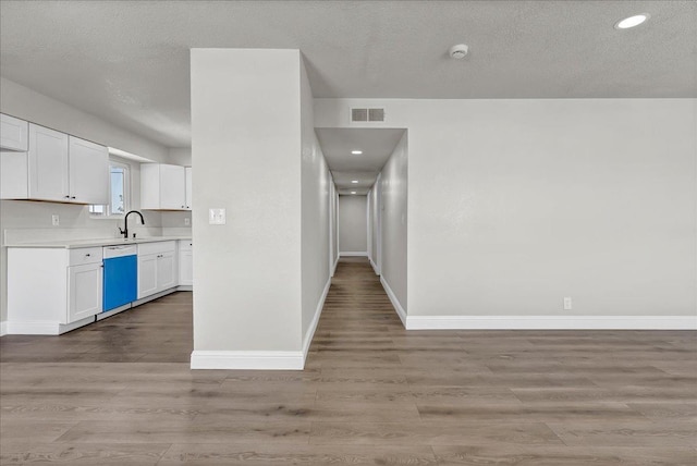 kitchen with dishwasher, light countertops, light wood-style flooring, white cabinets, and baseboards