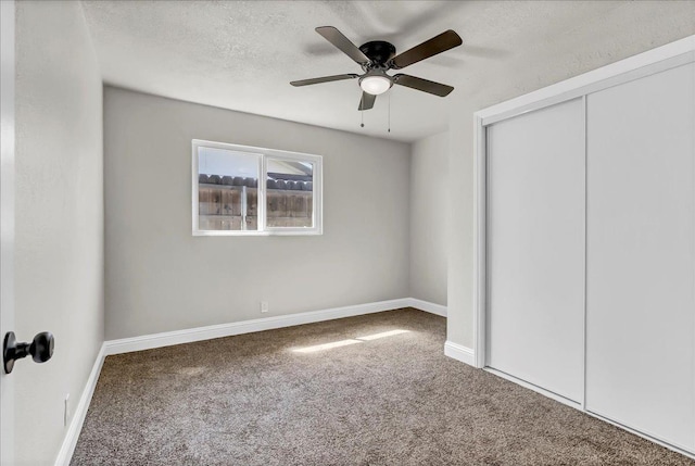unfurnished bedroom featuring carpet flooring, a closet, a textured ceiling, baseboards, and a ceiling fan
