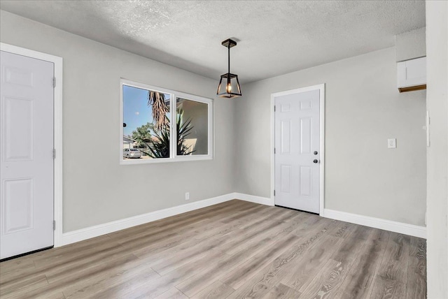 unfurnished dining area with wood finished floors, a textured ceiling, baseboards, and a chandelier