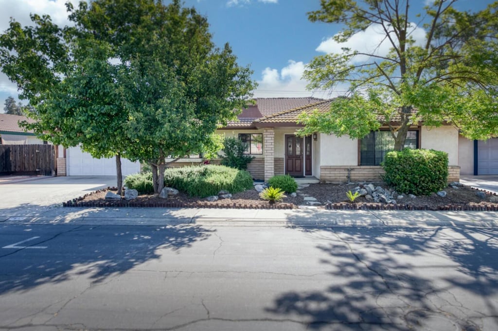 7664 N Gearhart Ave, Fresno, CA 93720 - view of property hidden behind natural elements featuring stucco siding, a tiled roof, driveway, and fence