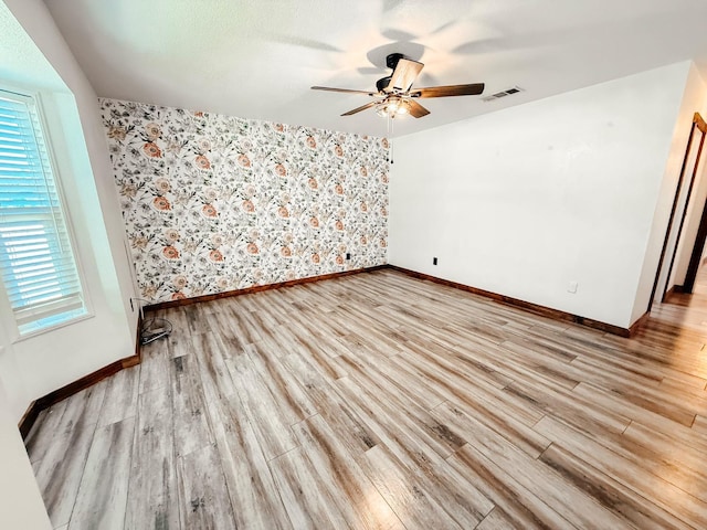 7784 S Del Rey Ave, Del Rey, CA 93616 - unfurnished room featuring baseboards, ceiling fan, wallpapered walls, light wood-style floors, and an accent wall