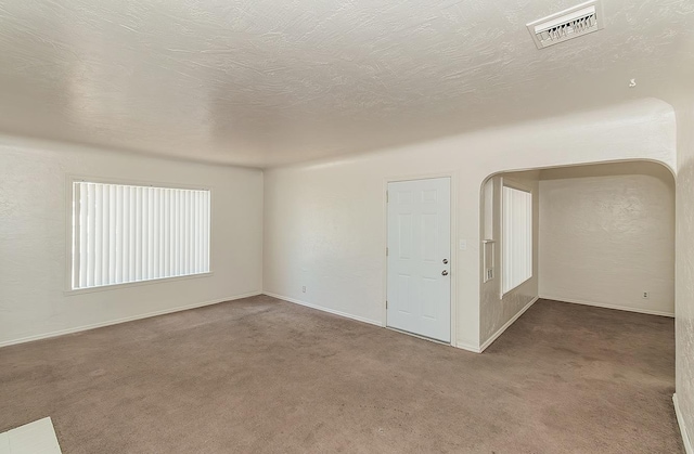 carpeted empty room featuring arched walkways and baseboards