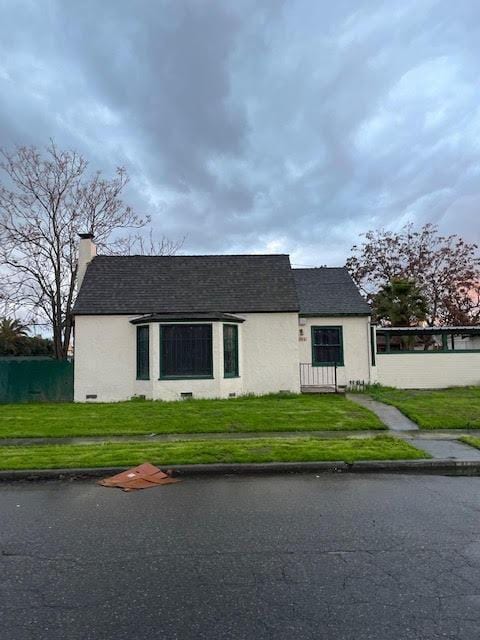 view of front facade featuring a front lawn, a chimney, stucco siding, and a shingled roof