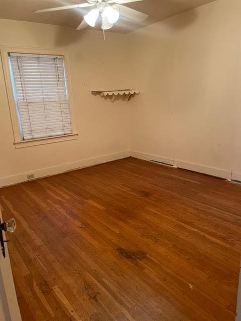 empty room with wood finished floors, a ceiling fan, and baseboards