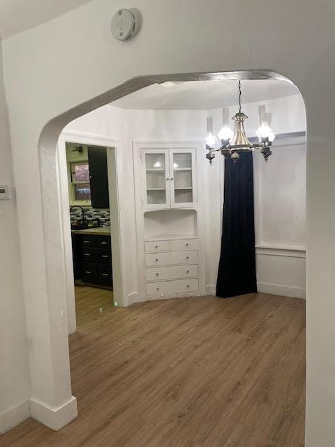 spacious closet featuring arched walkways, a chandelier, and wood finished floors