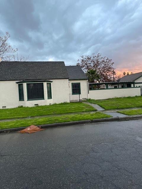 view of side of home with stucco siding, a lawn, and roof with shingles