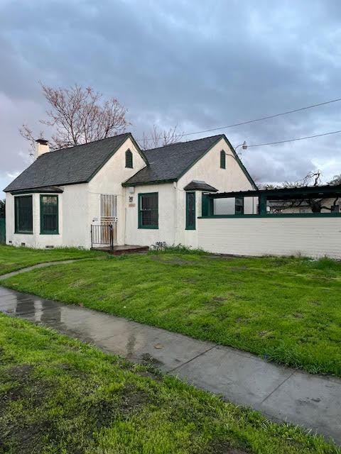 view of front of home with a chimney, a front yard, stucco siding, and roof with shingles