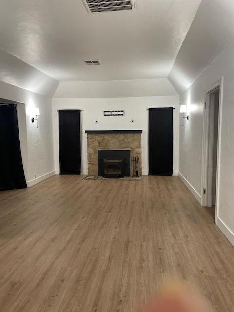 unfurnished living room featuring lofted ceiling, baseboards, wood finished floors, and a stone fireplace