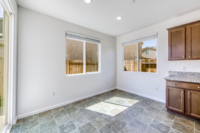 unfurnished dining area featuring baseboards, stone finish flooring, and recessed lighting