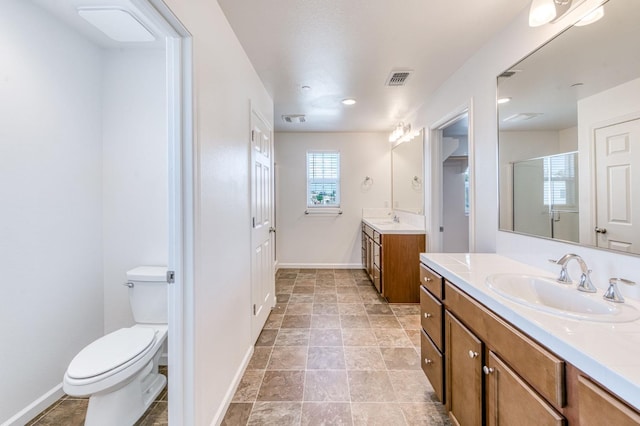 bathroom featuring baseboards, toilet, a shower stall, two vanities, and recessed lighting
