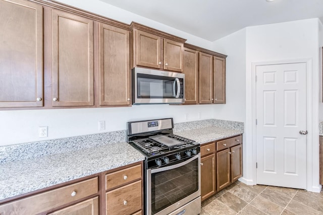 kitchen with appliances with stainless steel finishes, light stone countertops, and brown cabinets