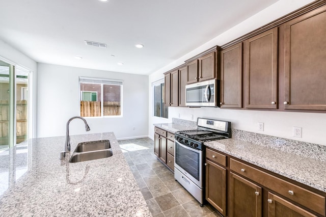 kitchen featuring stainless steel appliances, a sink, light stone countertops, baseboards, and recessed lighting