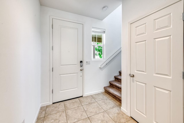 foyer entrance featuring baseboards, stairs, and light tile patterned floors