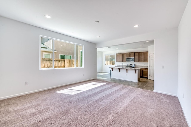 unfurnished living room featuring carpet, a sink, recessed lighting, and baseboards