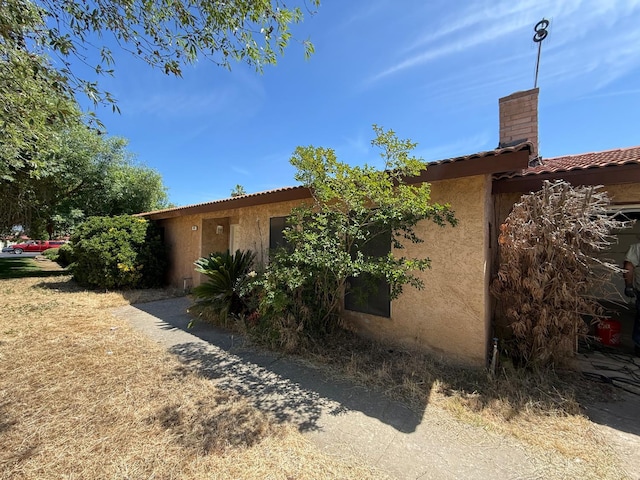 view of side of home with stucco siding, a tiled roof, and a chimney