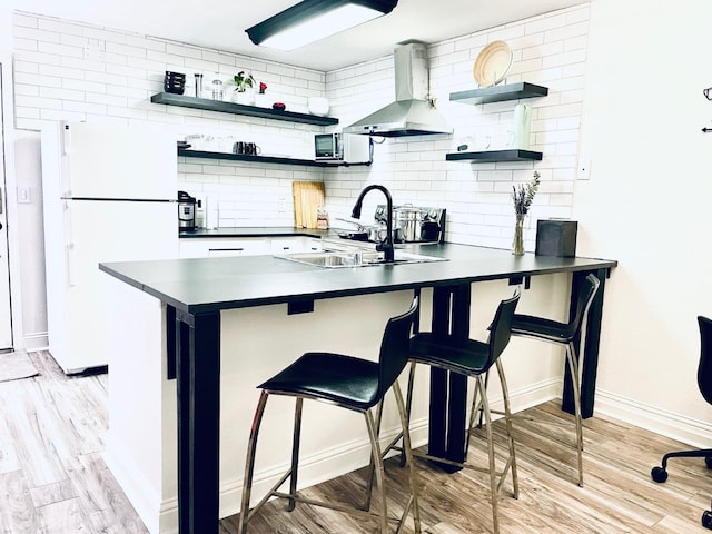 kitchen featuring open shelves, wall chimney range hood, freestanding refrigerator, and dark countertops