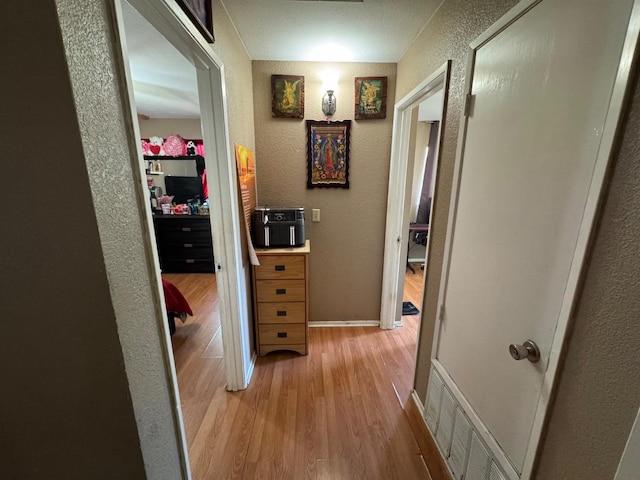 hall with a textured wall, light wood finished floors, and baseboards