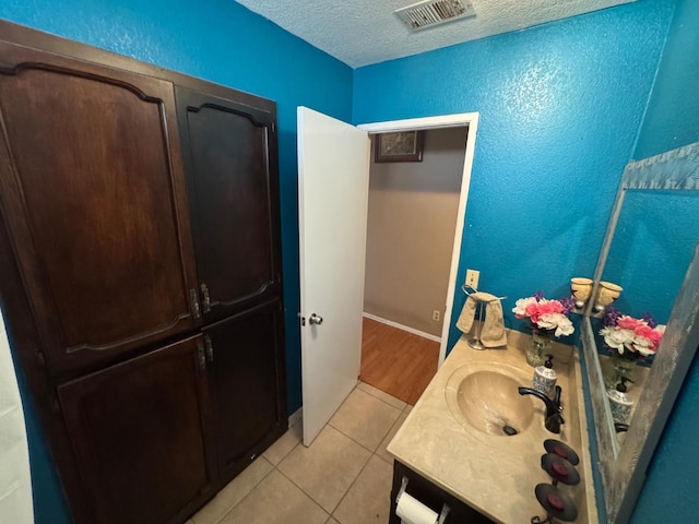 bathroom with tile patterned flooring, a textured ceiling, vanity, and a textured wall