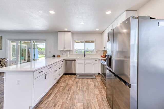 5932 E Illinois Ave, Fresno, CA 93727 - kitchen featuring appliances with stainless steel finishes, a peninsula, light wood-type flooring, healthy amount of natural light, and a textured ceiling