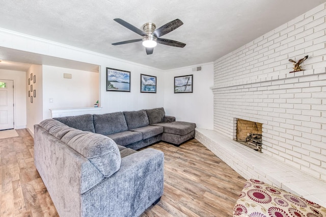 5932 E Illinois Ave, Fresno, CA 93727 - living room with wood finished floors, a ceiling fan, a textured ceiling, a brick fireplace, and ornamental molding