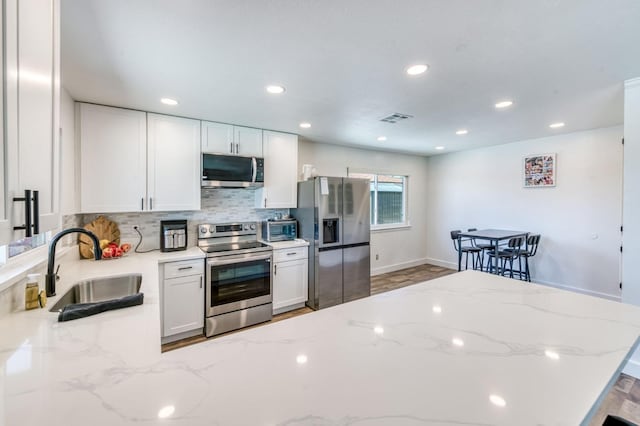 5932 E Illinois Ave, Fresno, CA 93727 - kitchen with stainless steel appliances, a sink, backsplash, white cabinets, and light stone counters