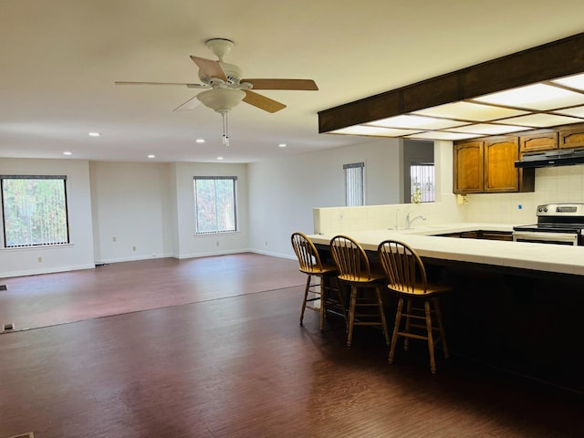 kitchen featuring stainless steel electric stove, under cabinet range hood, recessed lighting, decorative backsplash, and brown cabinets