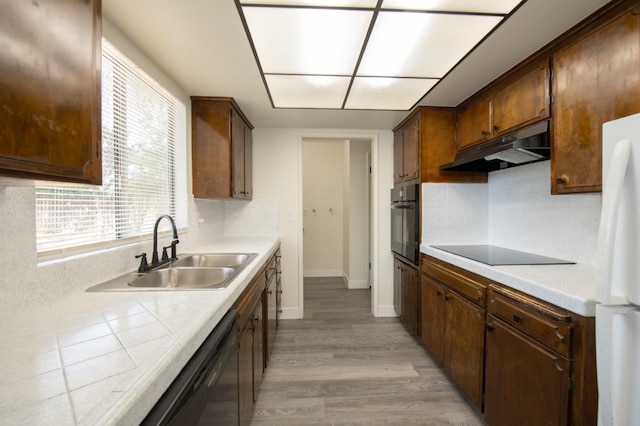 kitchen with under cabinet range hood, a sink, black appliances, light wood-style floors, and tasteful backsplash