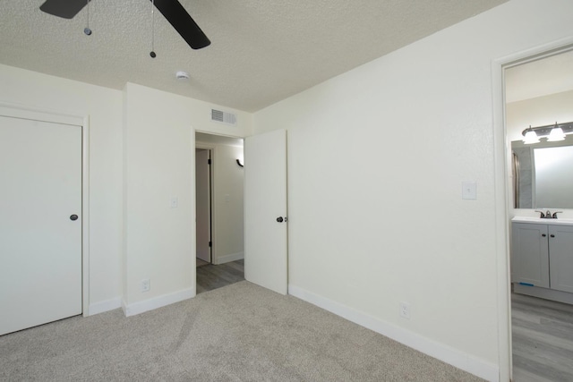 unfurnished bedroom with light colored carpet, baseboards, a sink, a textured ceiling, and ensuite bath