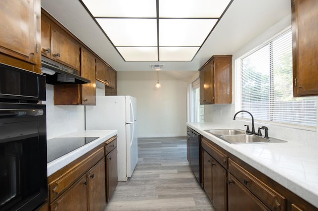 kitchen with a sink, black appliances, under cabinet range hood, light wood finished floors, and light countertops