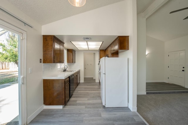 kitchen with freestanding refrigerator, vaulted ceiling, a sink, stainless steel dishwasher, and light countertops