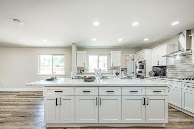 6117 N Colonial Ave, Fresno, CA 93704 - kitchen with wall chimney range hood, stainless steel double oven, light wood-style floors, tasteful backsplash, and recessed lighting