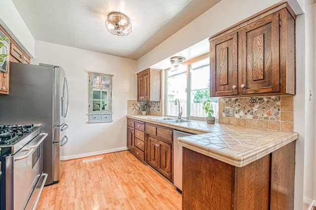 1487 W Paul Ave, Fresno, CA 93711 - kitchen featuring appliances with stainless steel finishes, tasteful backsplash, light wood finished floors, tile counters, and brown cabinetry