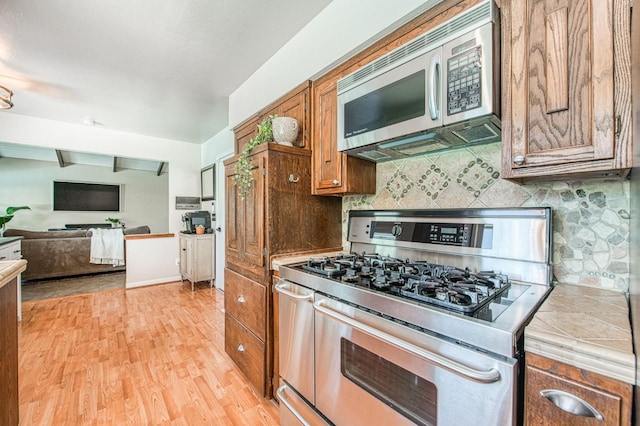 1487 W Paul Ave, Fresno, CA 93711 - kitchen featuring stainless steel appliances, brown cabinetry, light wood-style floors, decorative backsplash, and tile counters